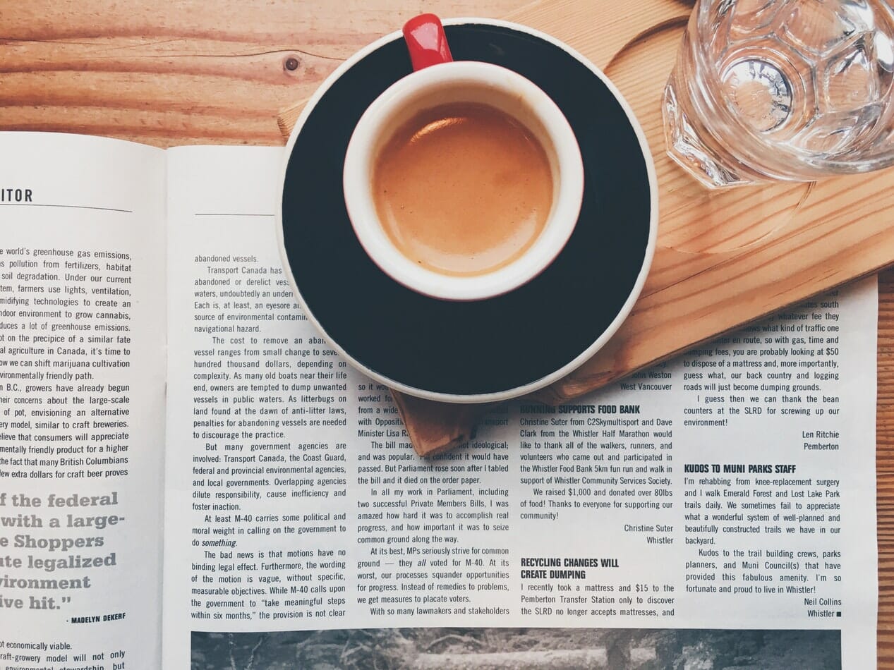 A cup of coffee and a newspaper on an insider's wooden table.