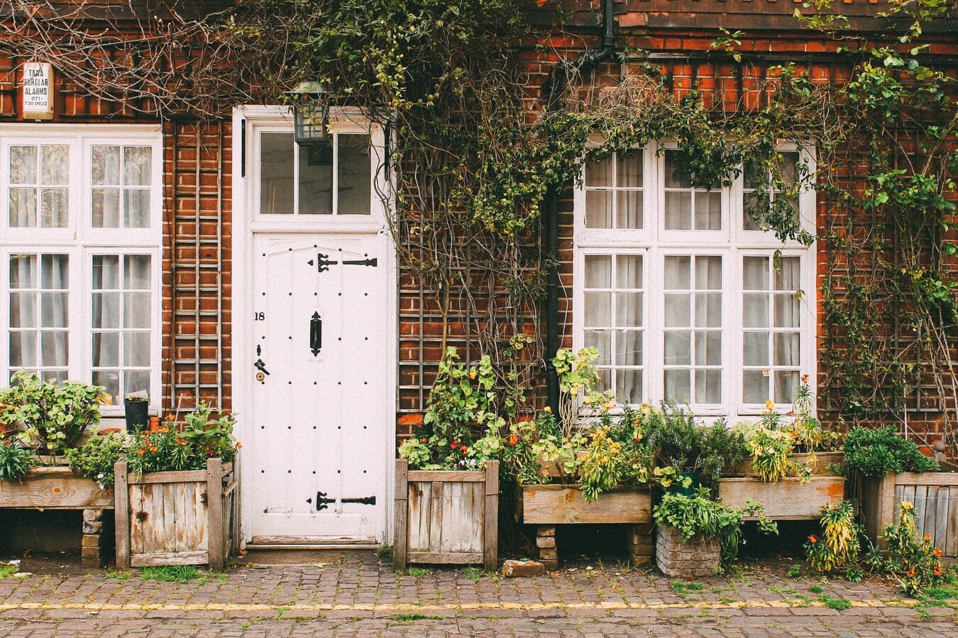 A white door with potted plants in front of a brick house.