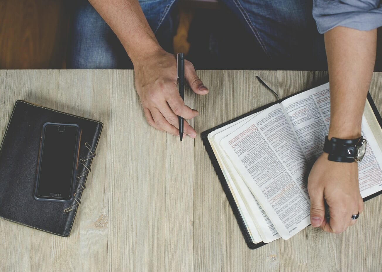 Two hands holding an open bible and a cell phone.