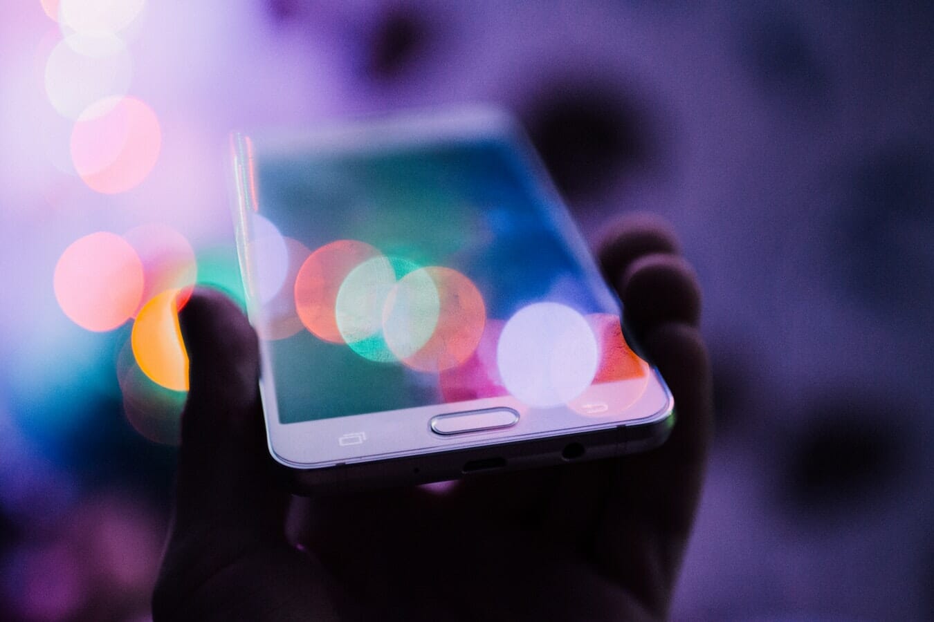 A person holding up a phone with bokeh lights.