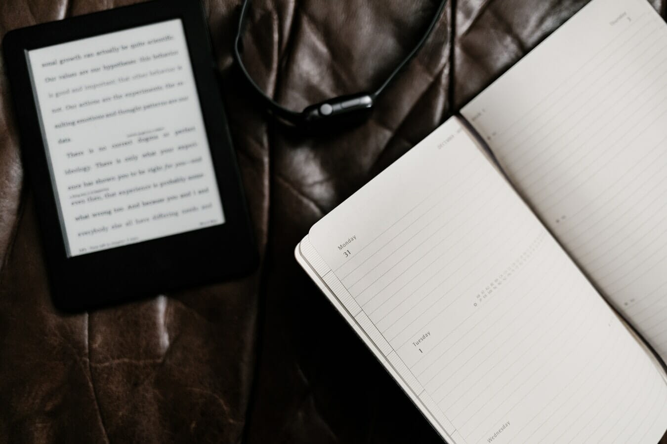 An open notebook and earphones on a leather surface.