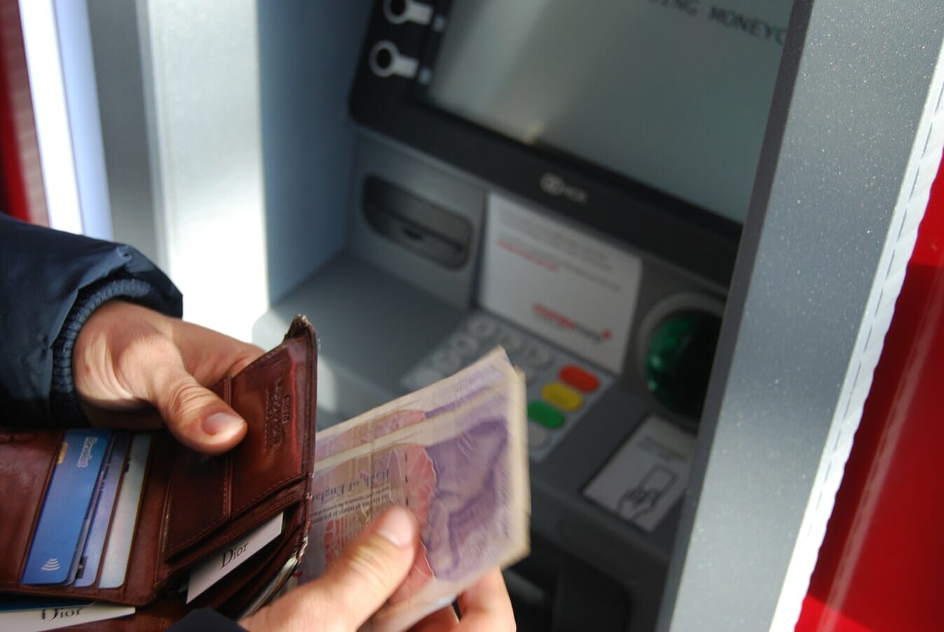 A person is holding a wallet and money in an atm machine.