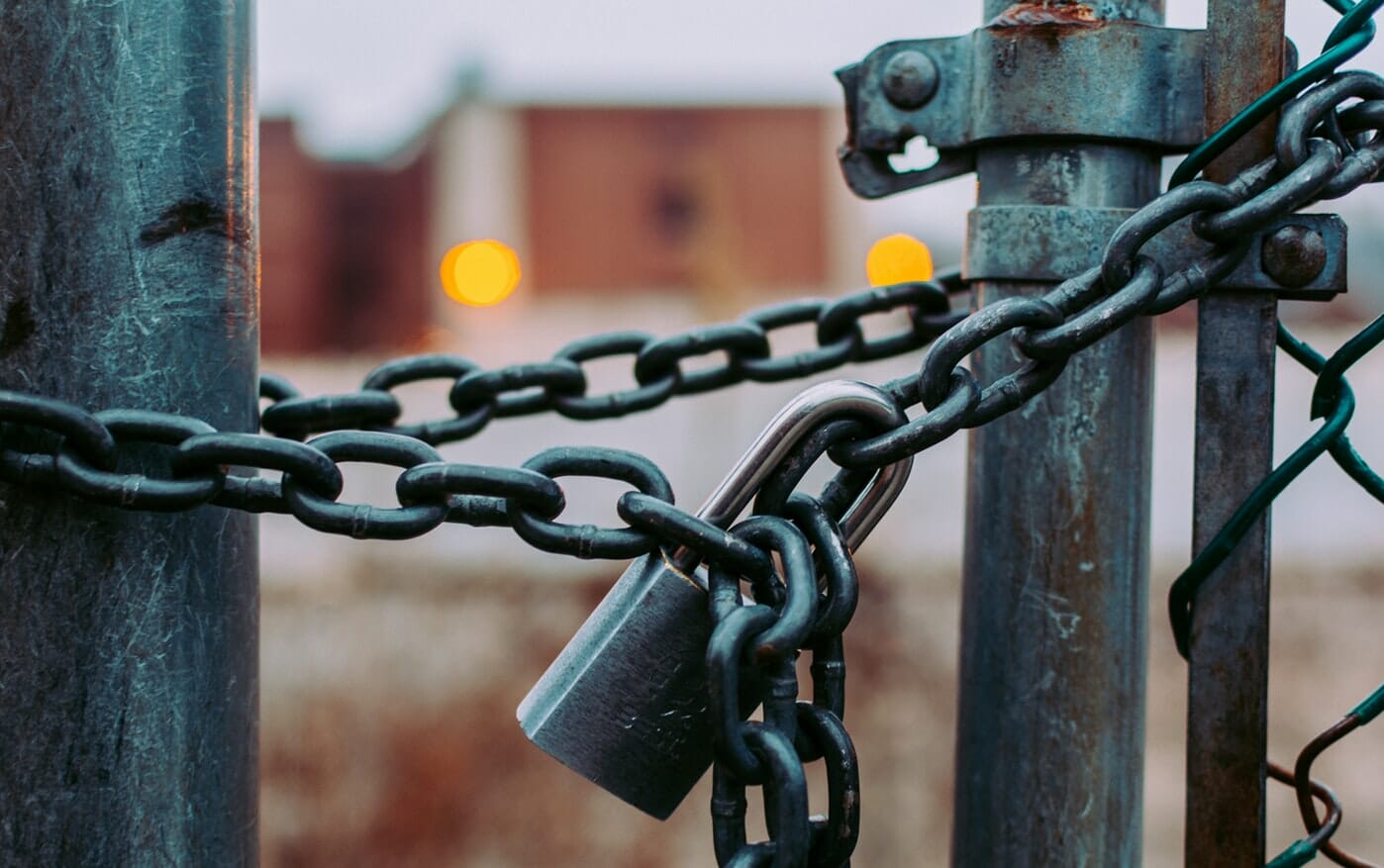 A chain with a padlock on it is attached to a fence.