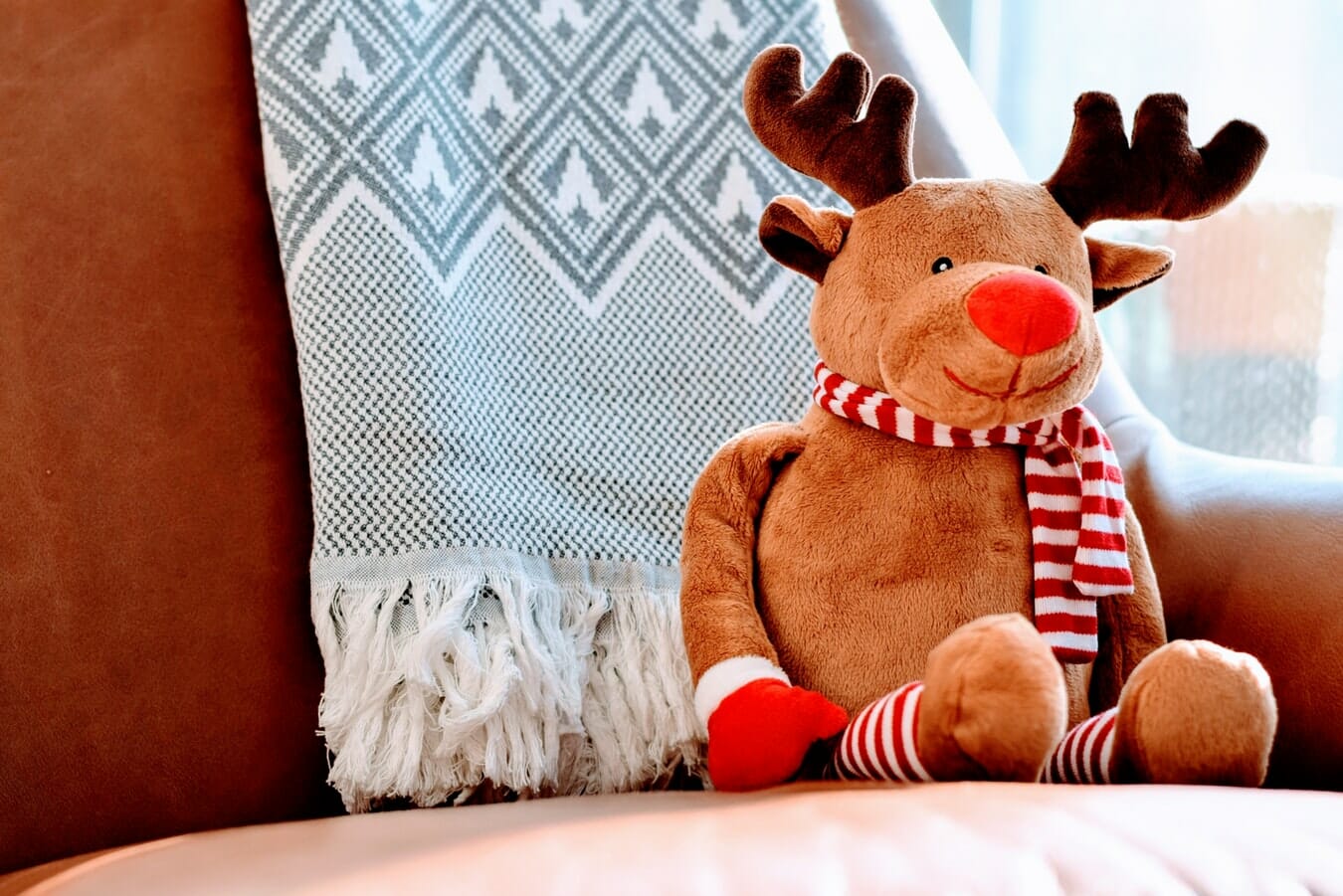 A stuffed reindeer sitting on a chair with a blanket.