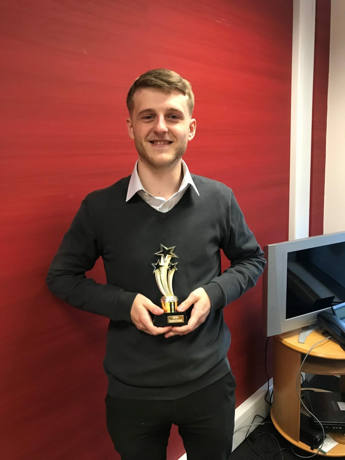 A man holding an award in front of a red wall.