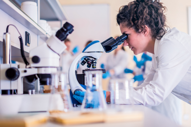 A woman is looking through a microscope in a lab.