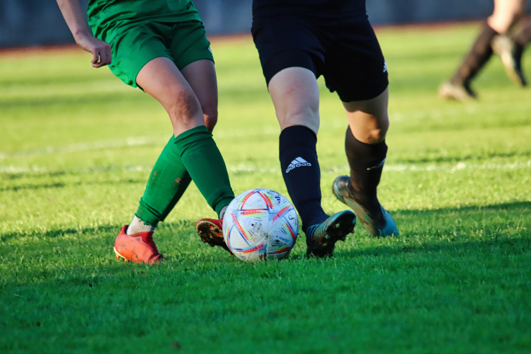 Two football players kicking the ball on a green field.
